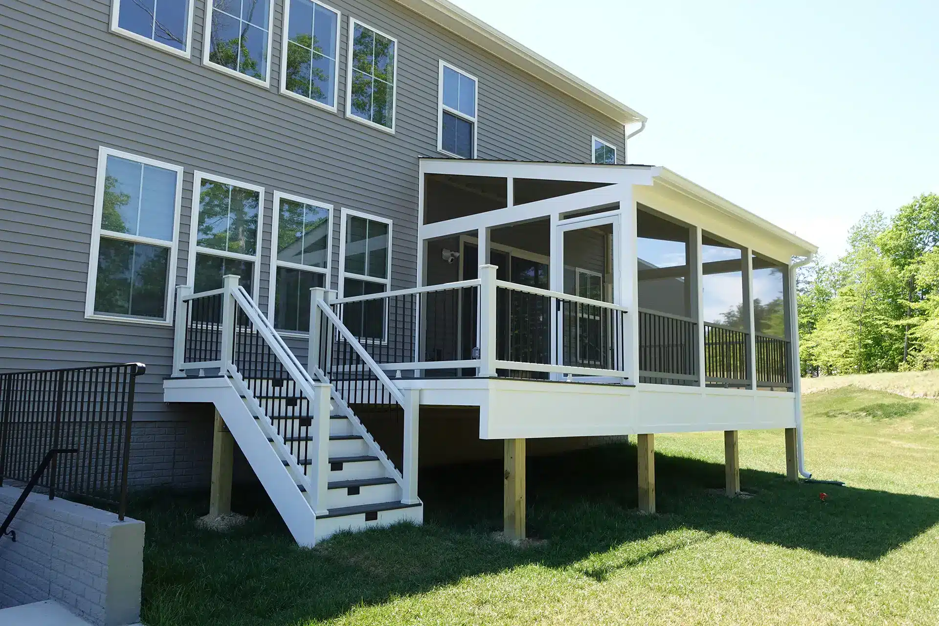 A large, two-story house in Lorton, VA, with gray siding features a white elevated deck and an attached screened-in porch. The deck includes white railings with black balusters and a set of white stairs leading down to a grassy yard.
