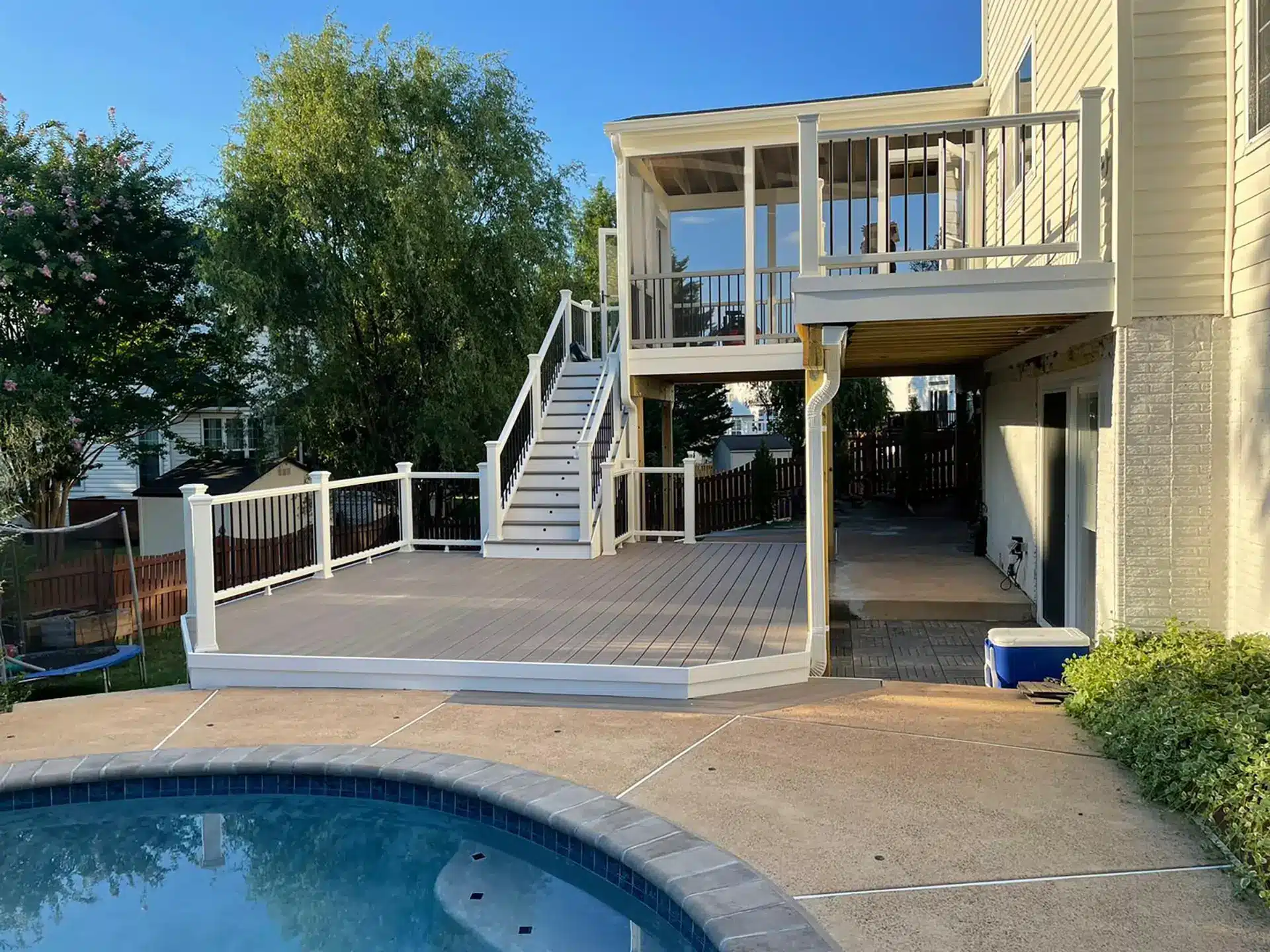 Multi level composite deck with gray decking, white railings, black balusters, stairs, and a screened porch overlooking a backyard swimming pool.