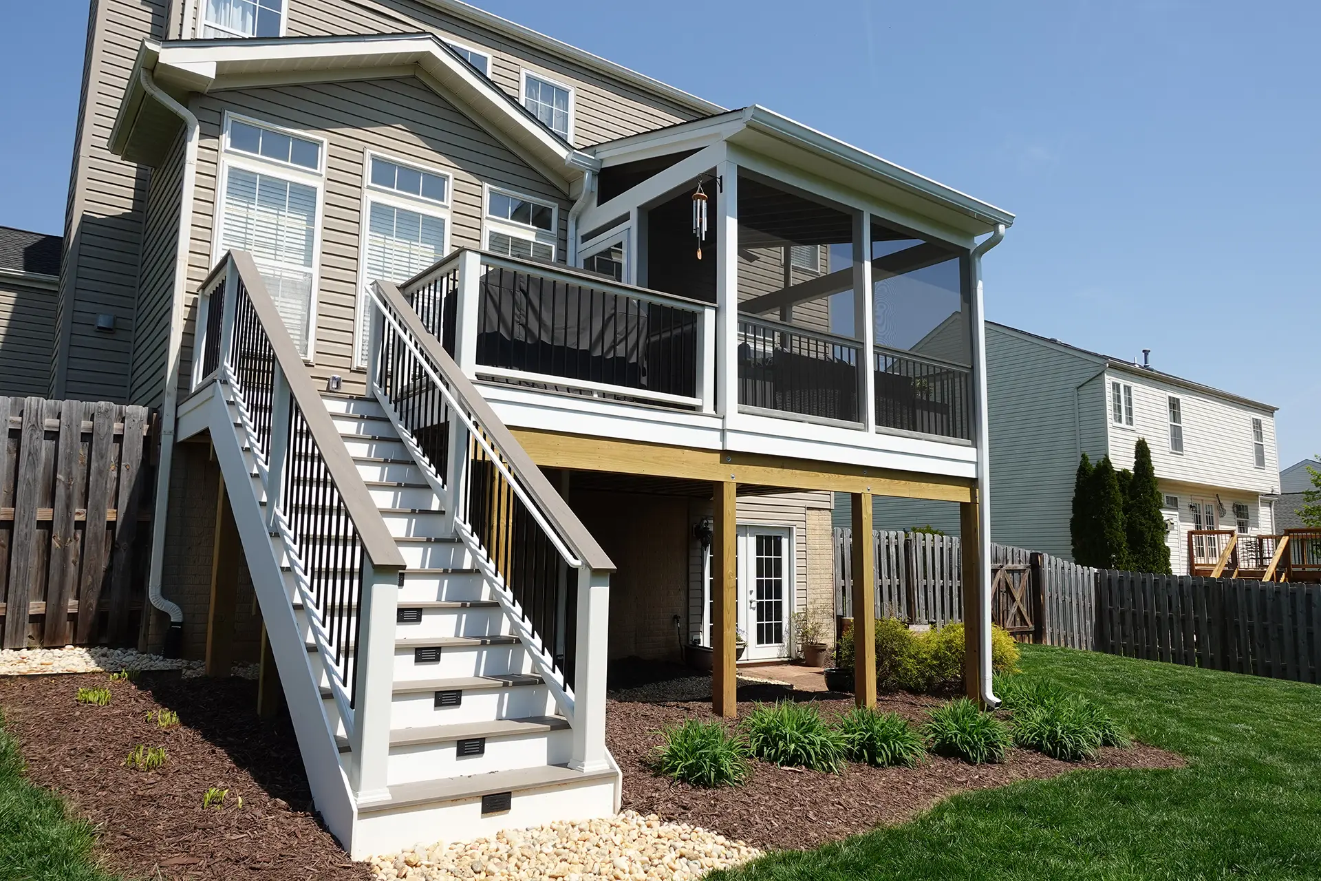 An elevated composite deck with a white staircase and a screened-in porch attached to a two-story tan house in Franconia, VA.