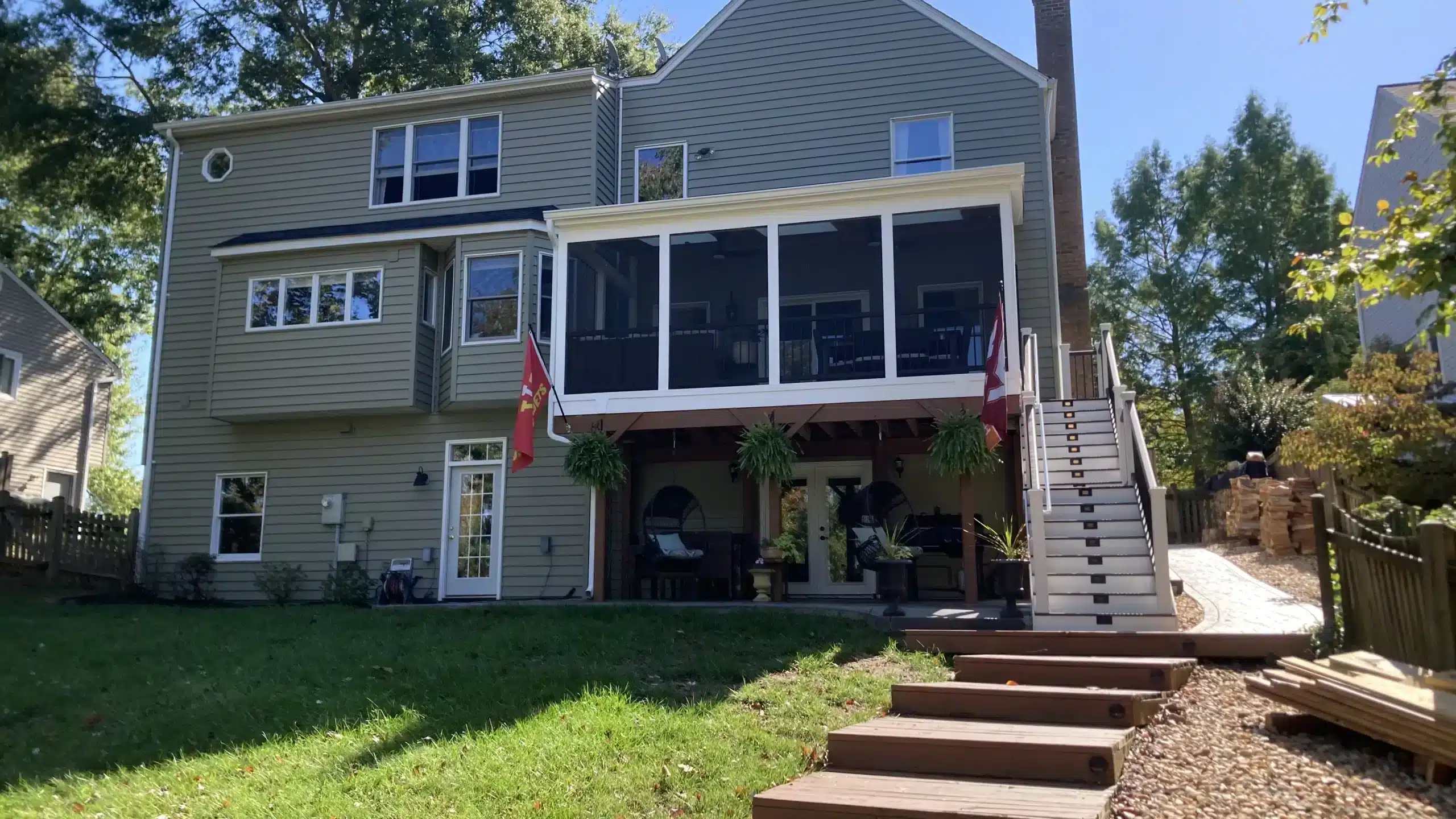 deck construction in fort washington md Raised screened porch with white framing, black railings, exterior stairs, and a covered patio beneath overlooking a landscaped backyard.