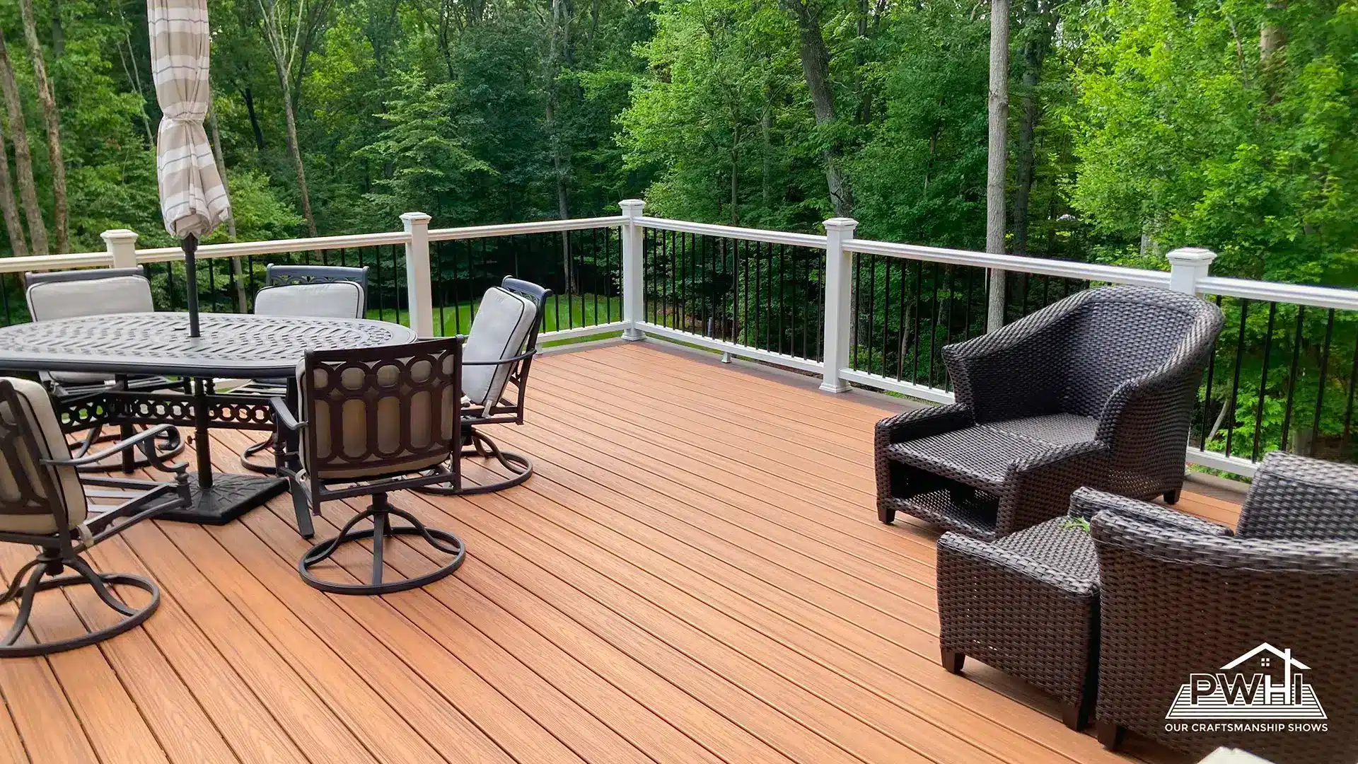 deck construction in reston va Composite deck with warm wood tone decking, white posts, black balusters, outdoor dining furniture, and wicker seating overlooking a wooded backyard.