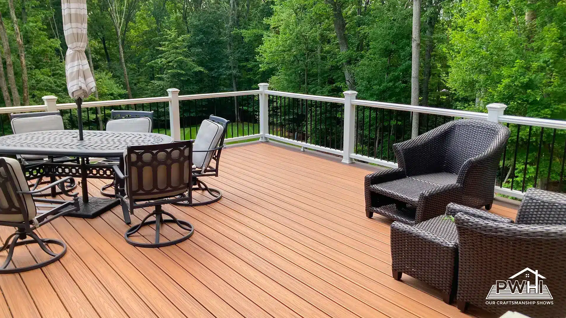 deck construction in rockville md Composite deck with warm wood tone decking, white posts, black balusters, outdoor dining furniture, and wicker seating overlooking a wooded backyard.