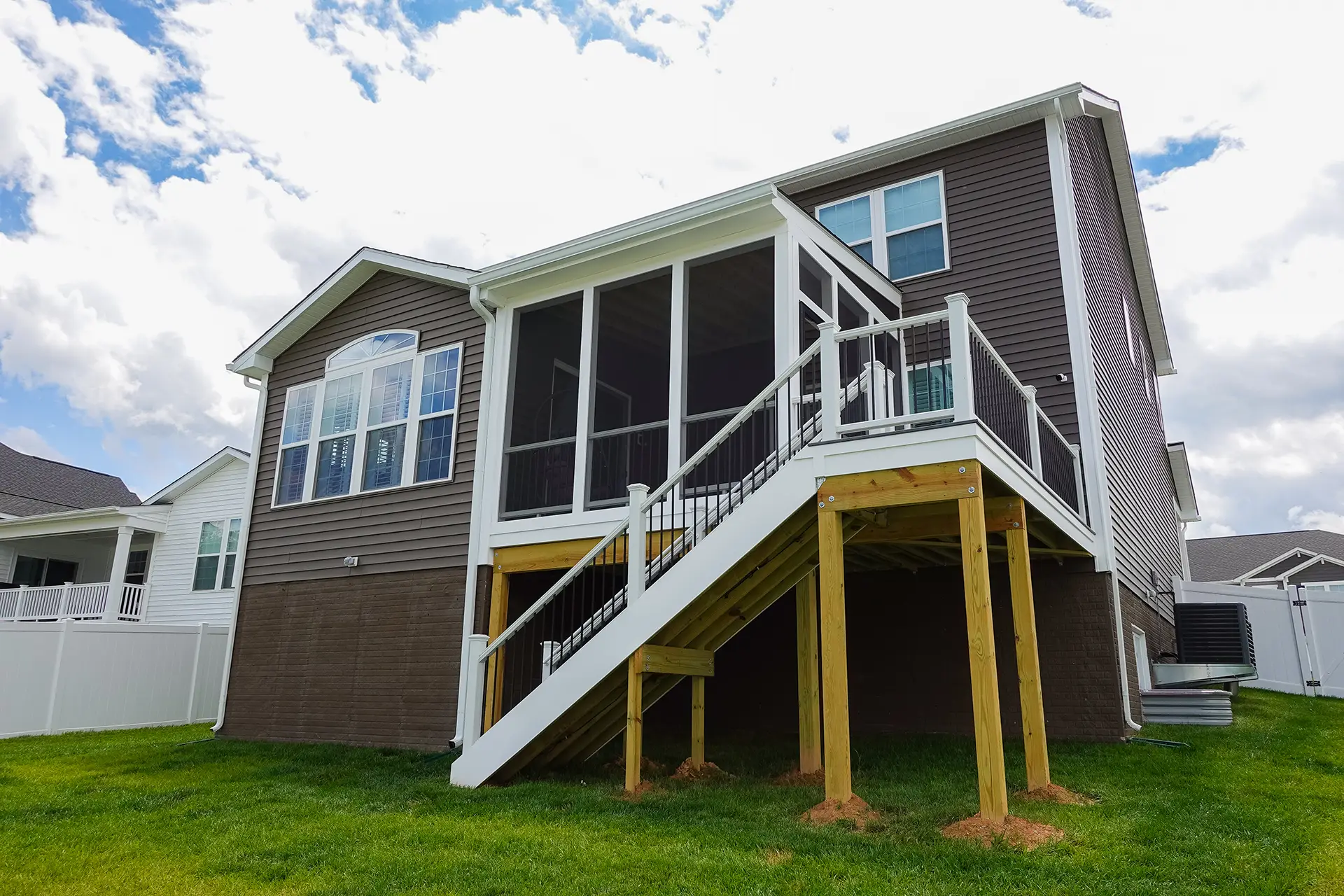 Elevated screened porch, white framing, black railings, and a long staircase attached to the back of a two-story home.