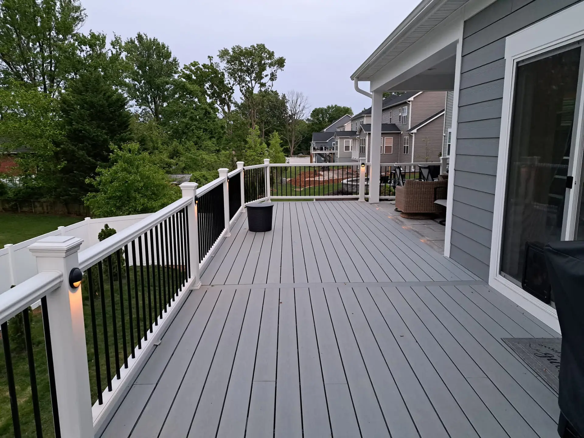 deck contractor in stafford va Composite deck with gray decking, white railings, black balusters, built in post lights, and a covered seating area beside the home.