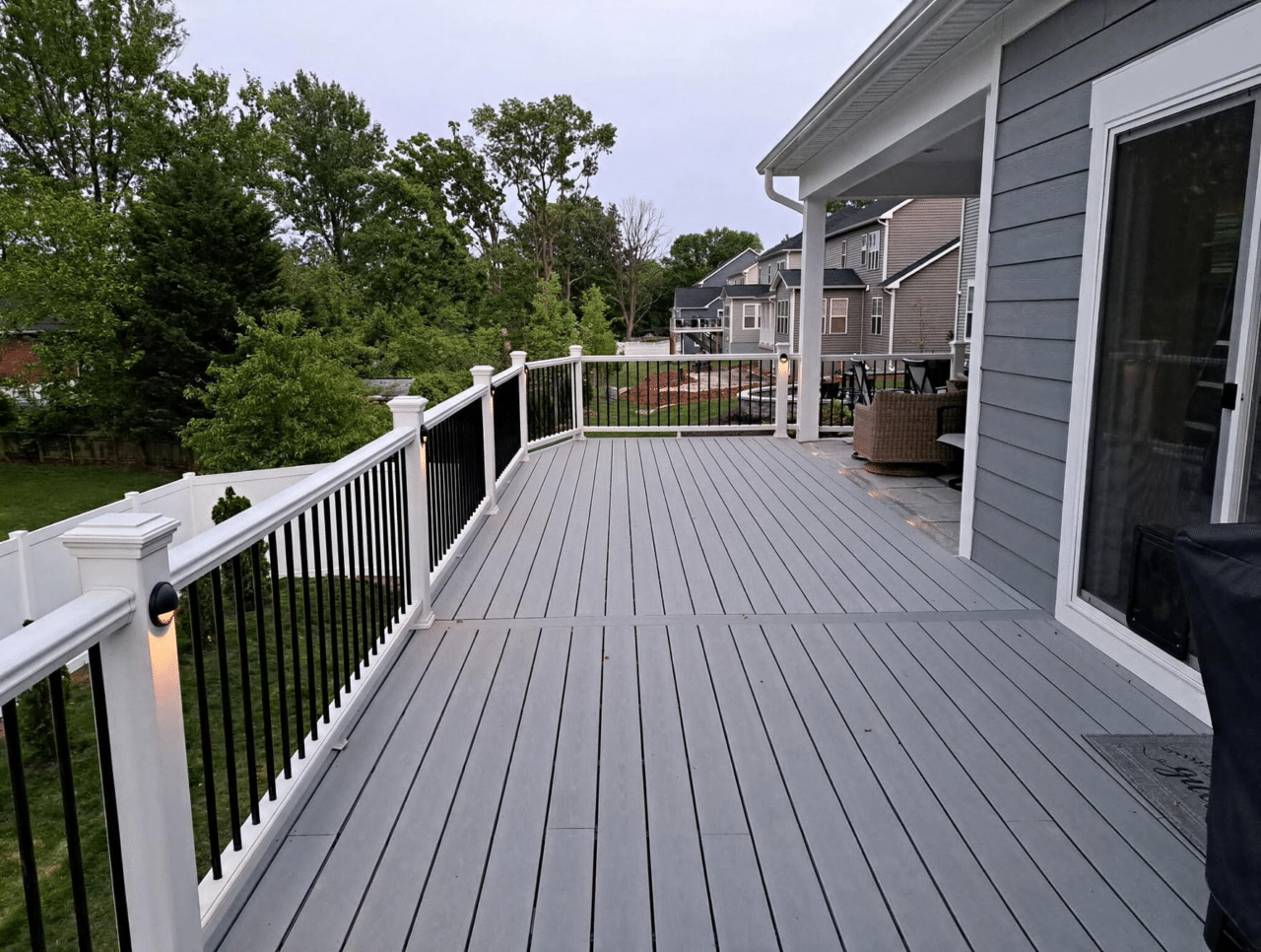 Gray composite deck with white posts, black railings, and an attached screened porch overlooking a backyard by Prince William Home Improvement.