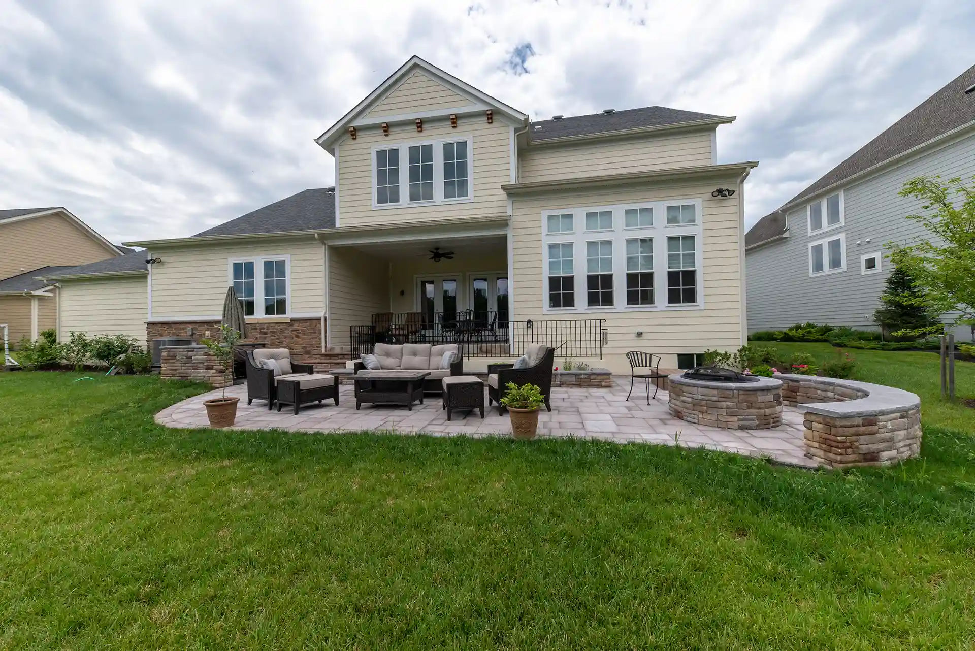 Backyard patio with a built-in fire pit, outdoor seating, and a covered deck area attached to a modern beige home.
