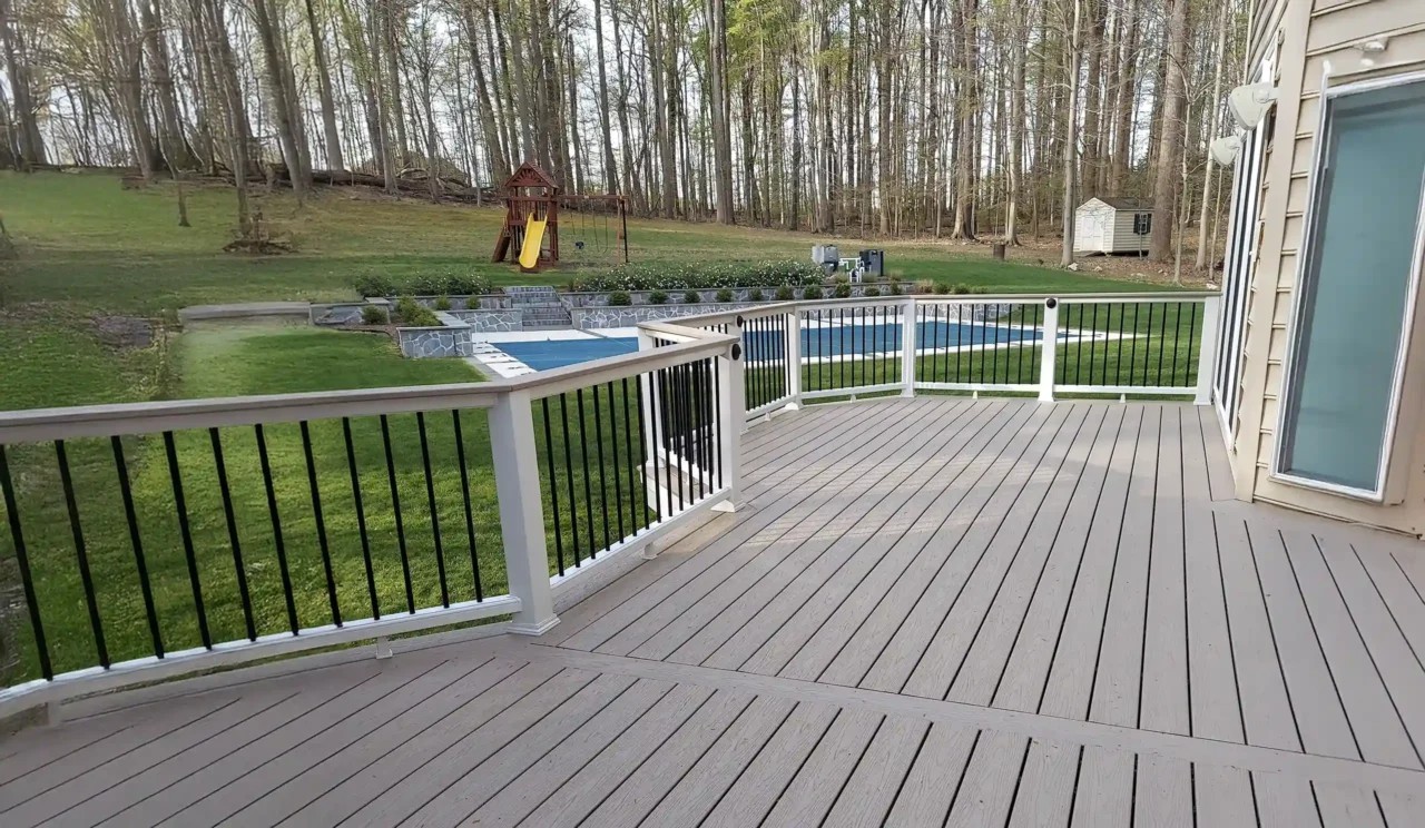 Modern composite deck with white and black railing overlooking a green backyard with a pool and wooded area - Spring Deck Building Ideas - Expert Deck Builders in Virginia