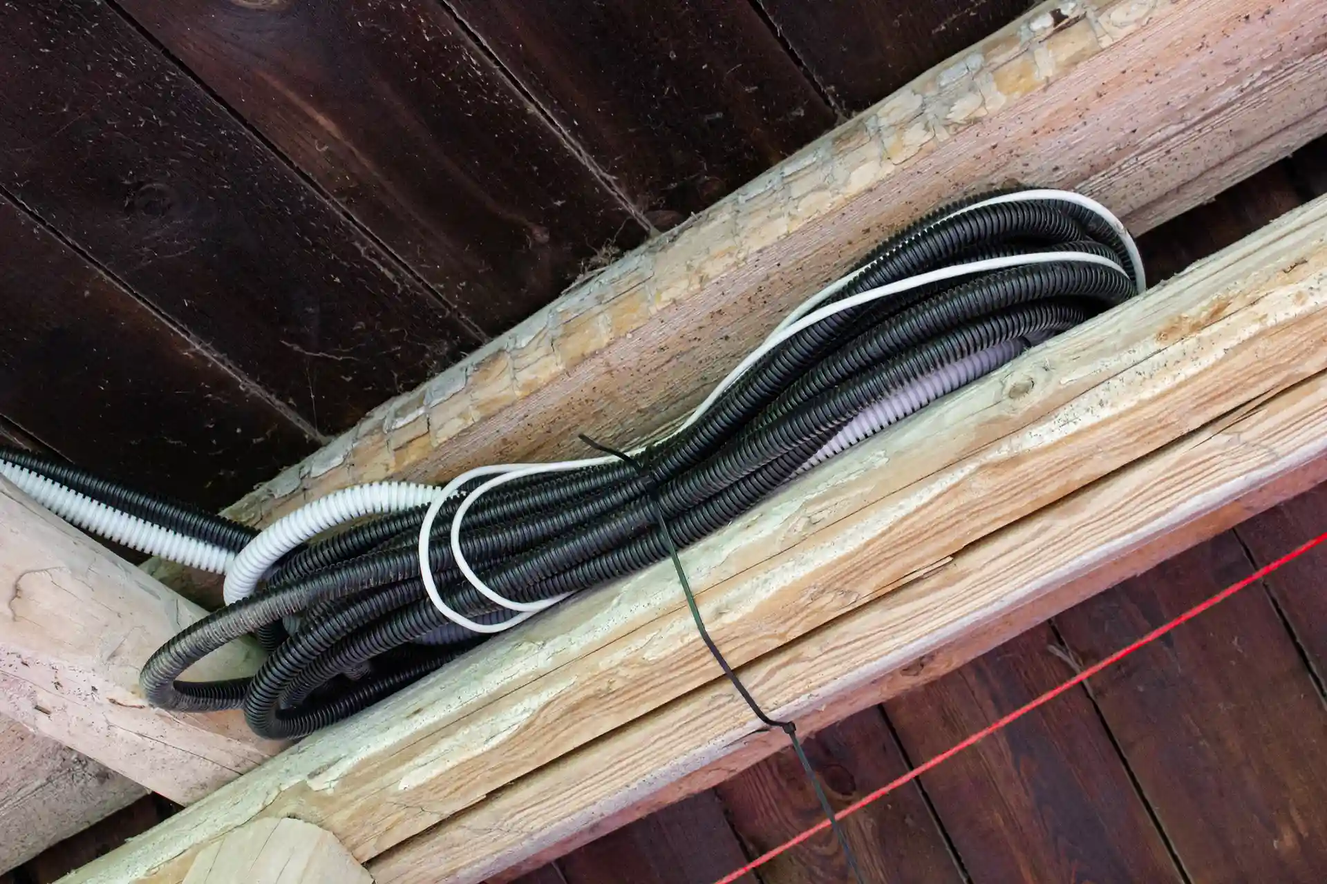 Electrical cables secured above wooden beams.
