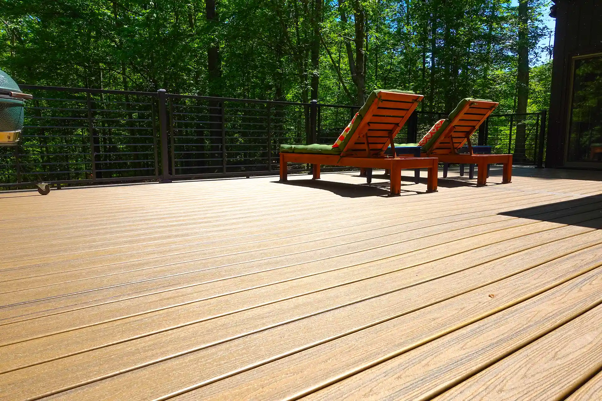 Composite deck with two lounge chairs, cable railing, and surrounding wooded area. 