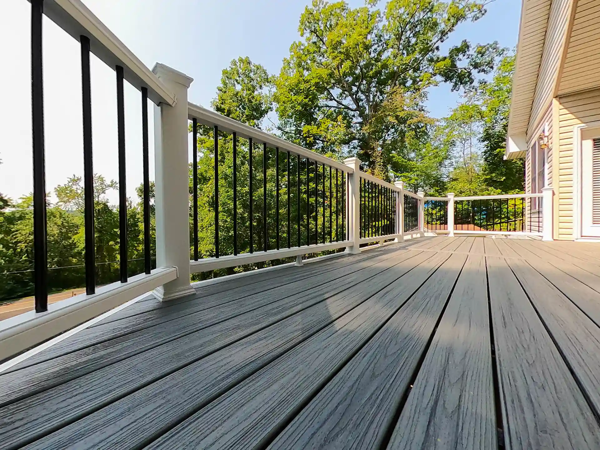 Gray composite deck with white and black railing attached to a house, surrounded by trees 