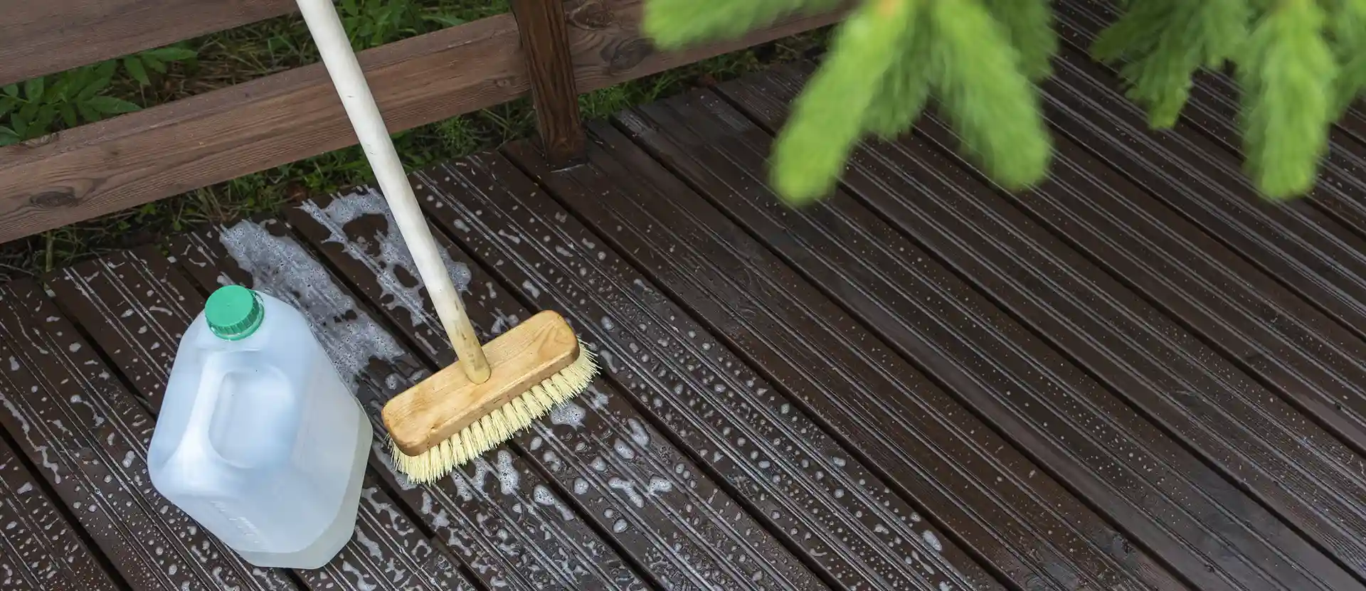 Deck being cleaned with a broom and cleaning solution, with water droplets on the surface.
