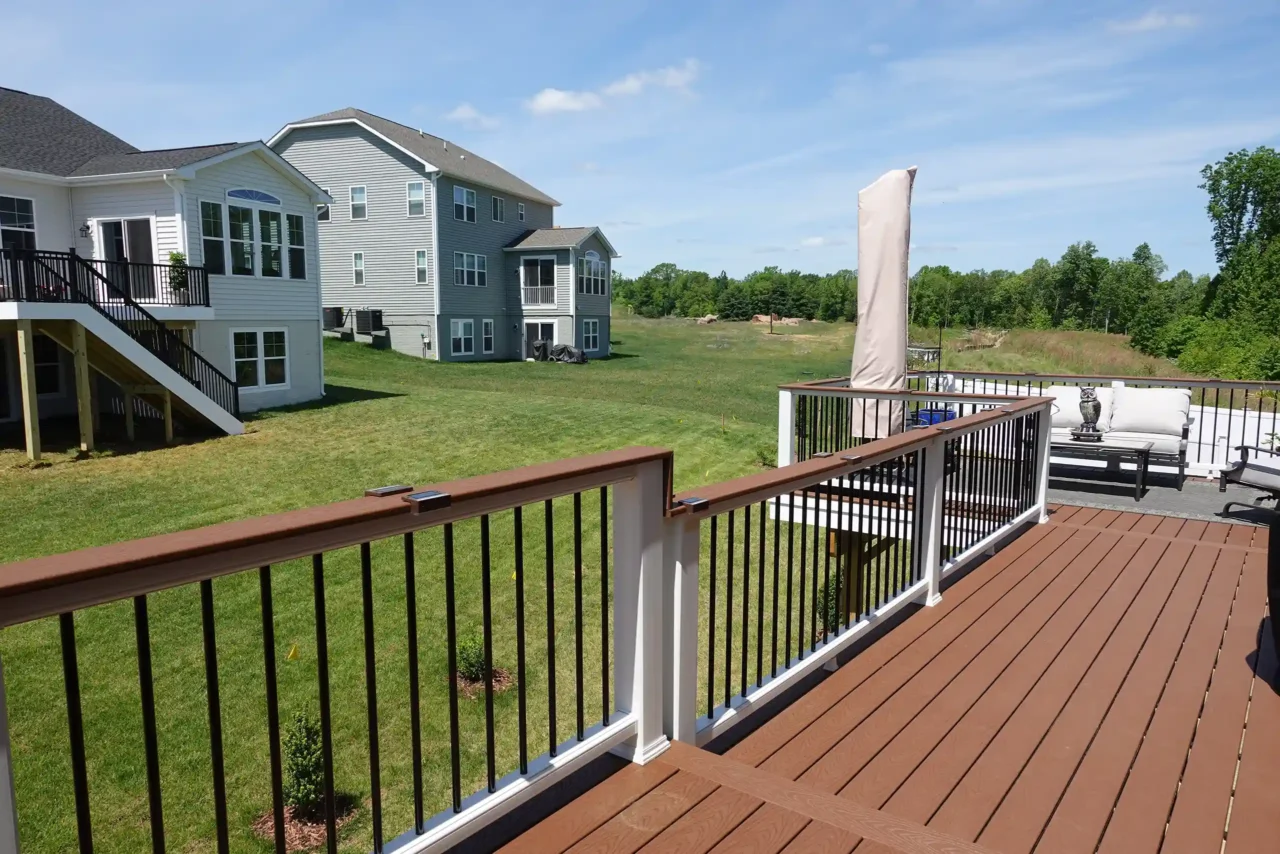 Deck with composite wood flooring and metal railings overlooking a grassy backyard with neighboring houses.
