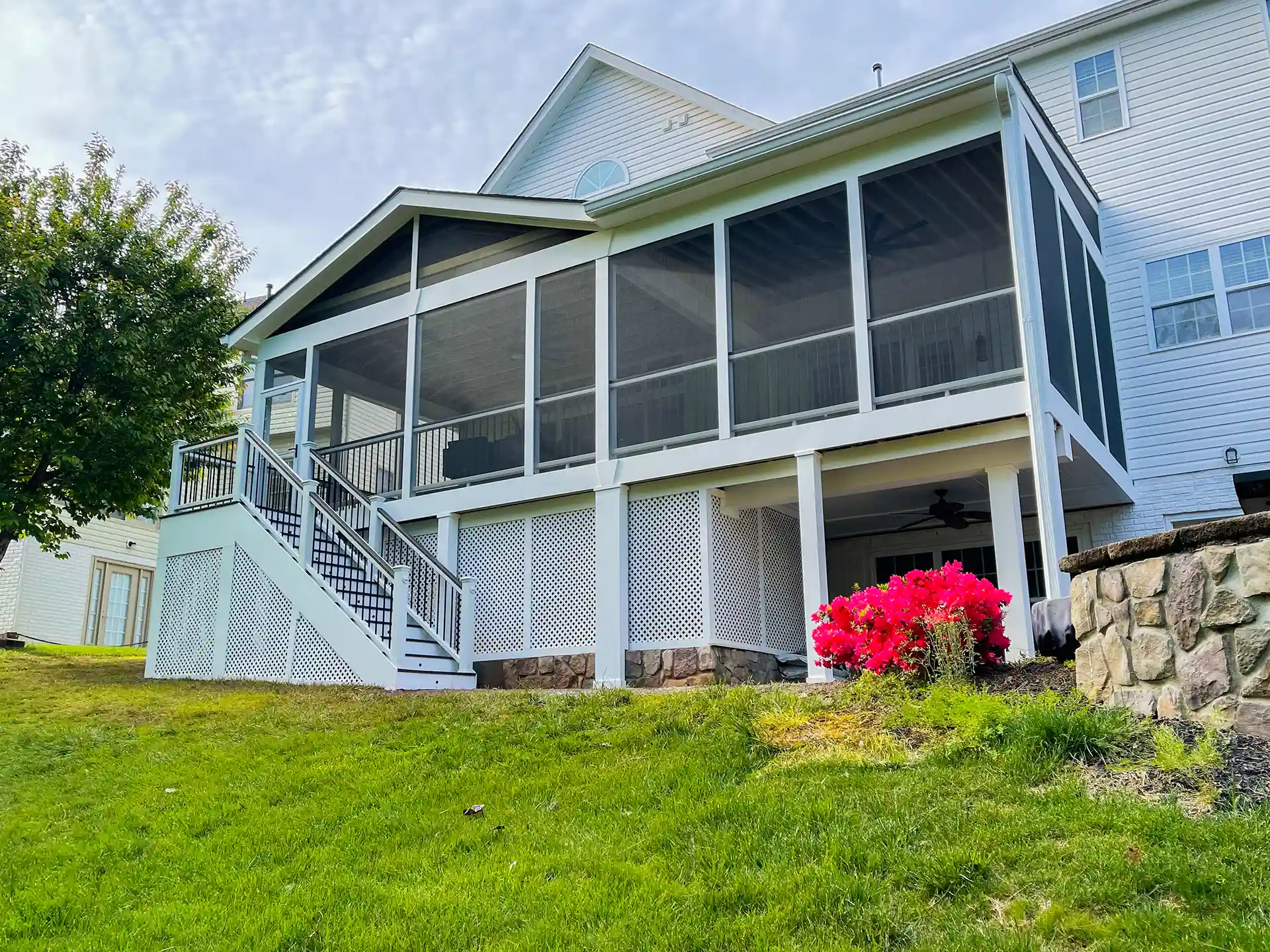 Screened-in deck with stairs leading up to it, surrounded by lattice and vibrant flowers in the foreground. 