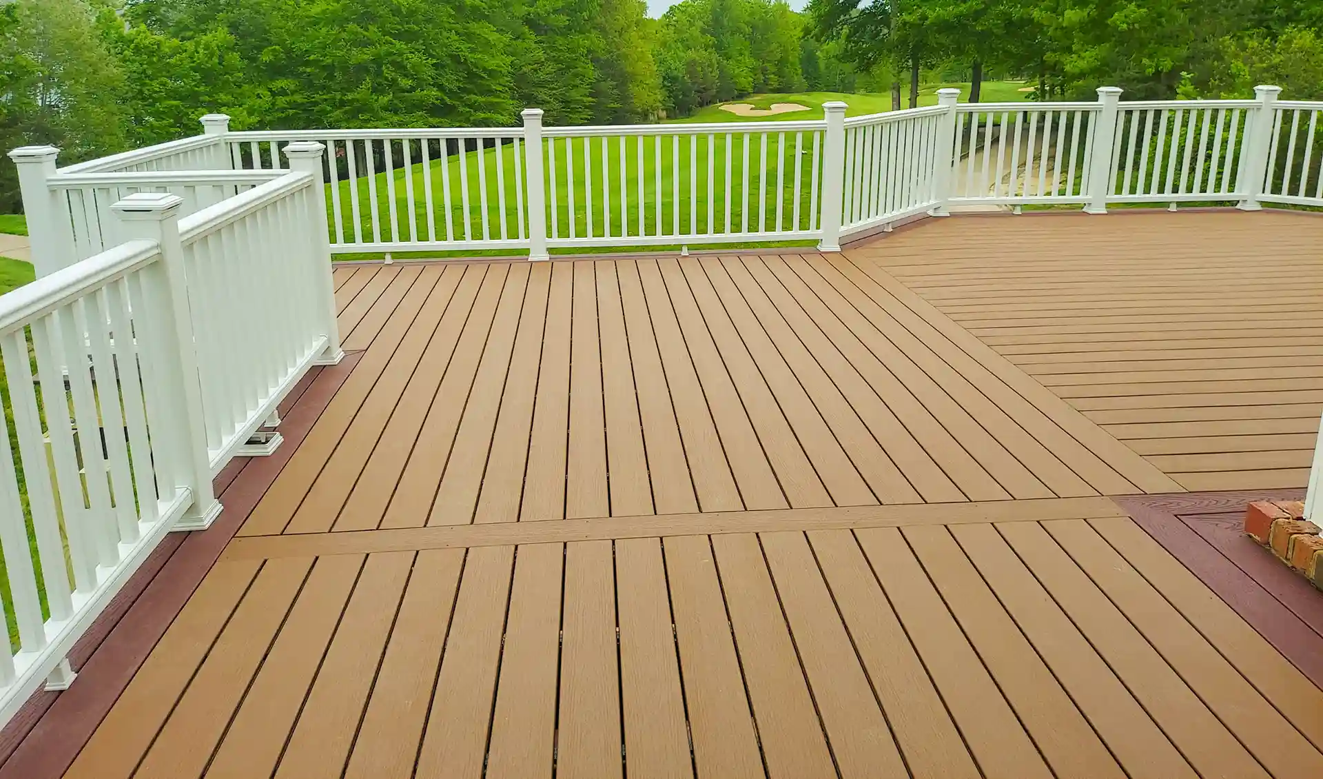 Spacious composite deck with white railings overlooking a lush green golf course and trees.
