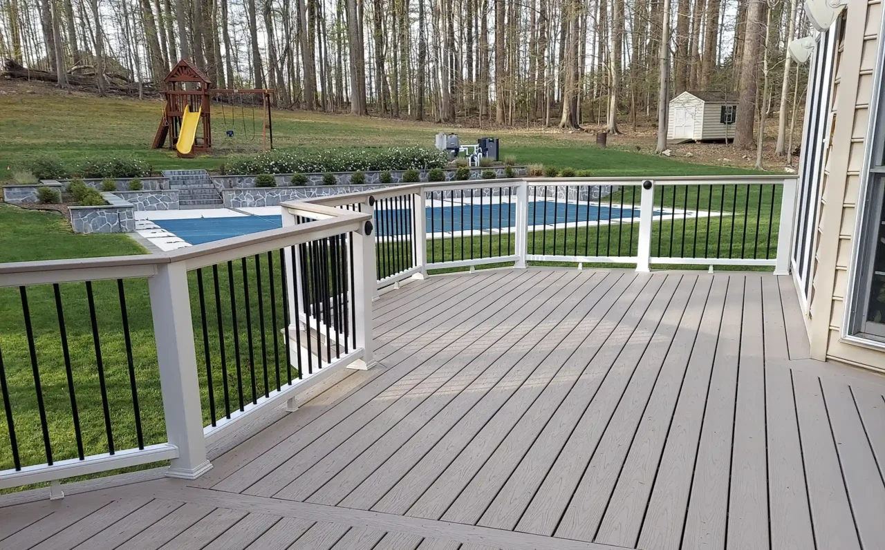 A deck with white railing and composite decking, overlooking a backyard with a playground and pool.