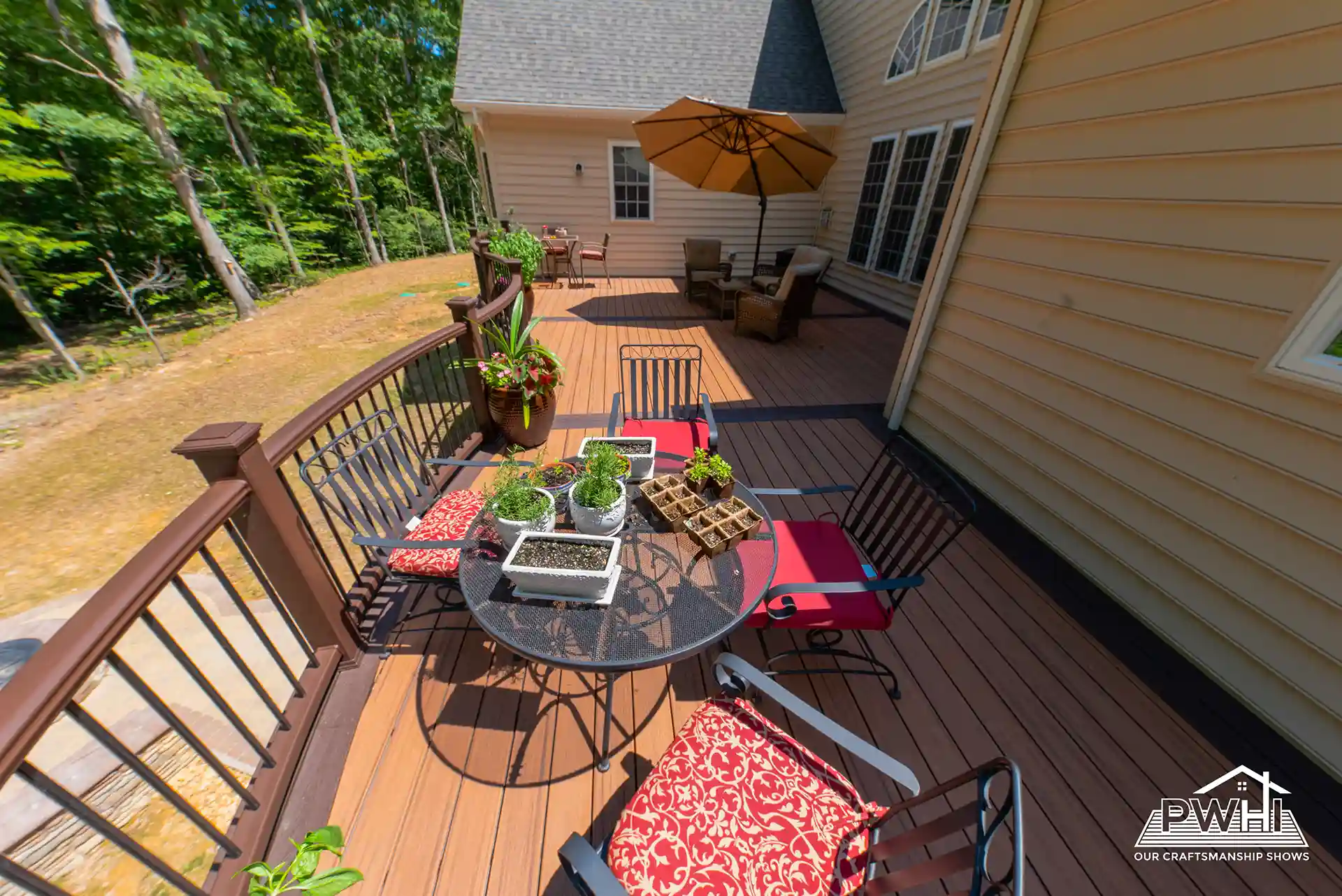 Outdoor deck with composite flooring, black railing, and a dining table with potted plants, chairs, and an umbrella. 
