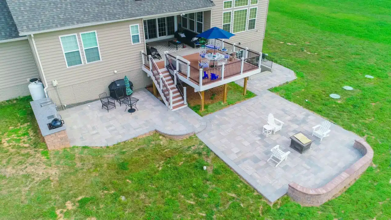 Aerial shot of a deck connected to a paver patio, featuring seating, a fire pit, and open lawn space.