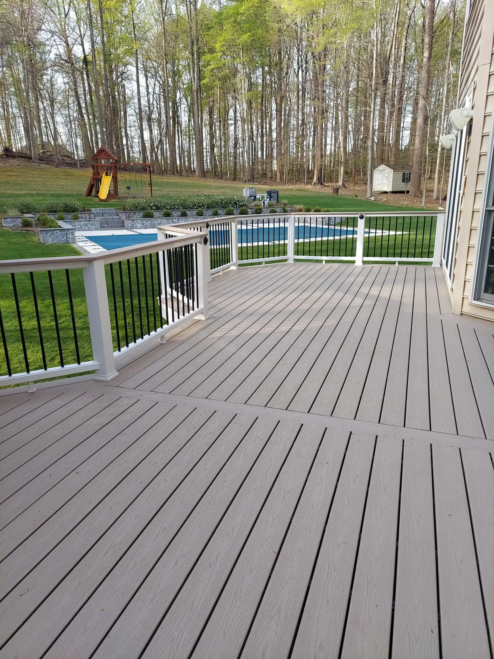 Composite deck with railing A composite deck with light-colored decking and black railing with a view of a backyard with a playground.