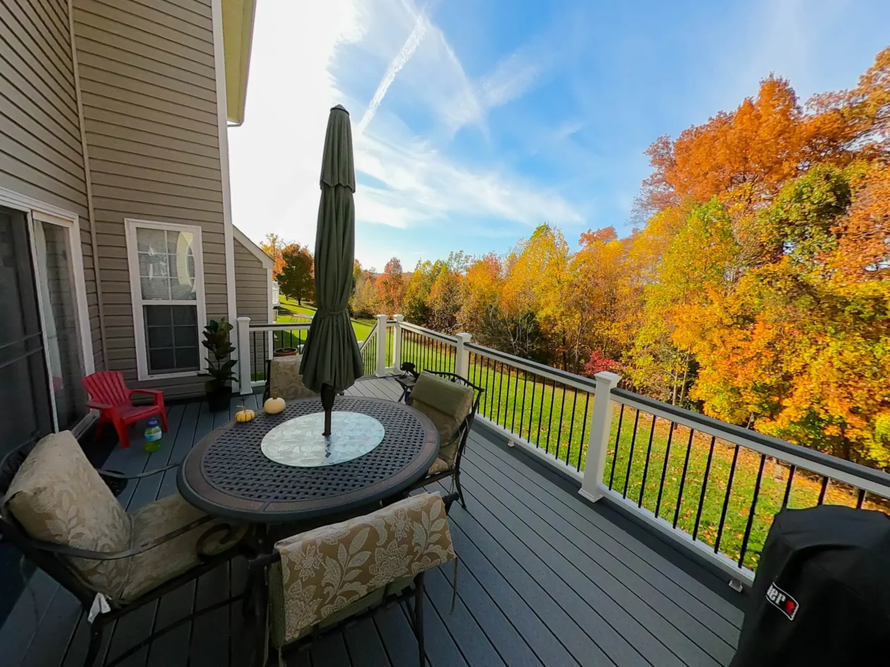 A deck with a table and chairs, a grill, and a scenic autumn landscape in the background, featuring colorful fall foliage.
