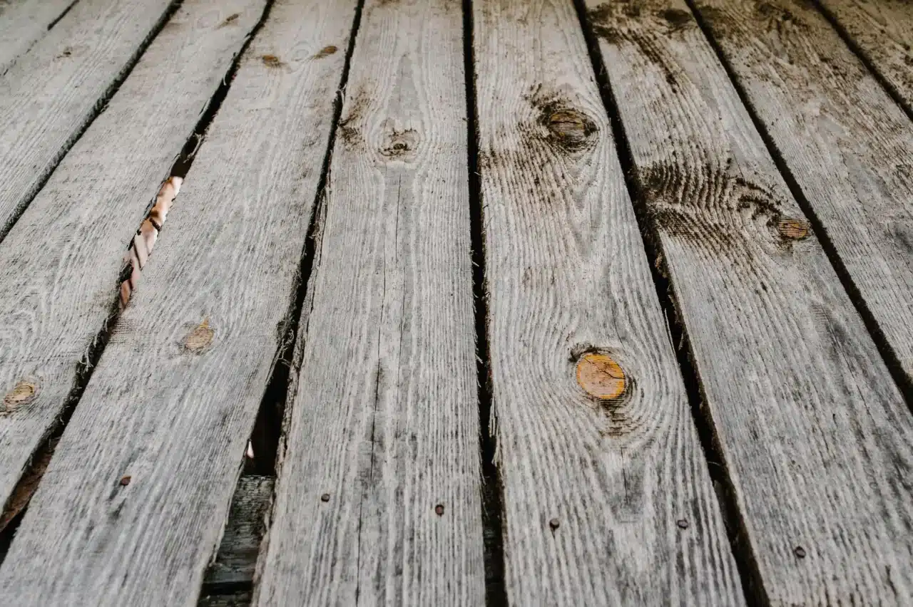 Close-up of weathered wooden deck boards with visible gaps, cracks, and knots.