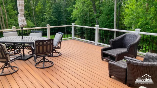 Why Prince William Home Improvement is the Right Choice for Your Deck 2 A deck made of composite material with a dining table, chairs, and wicker seating. The deck has white and black metal railings, overlooking a green, wooded area.