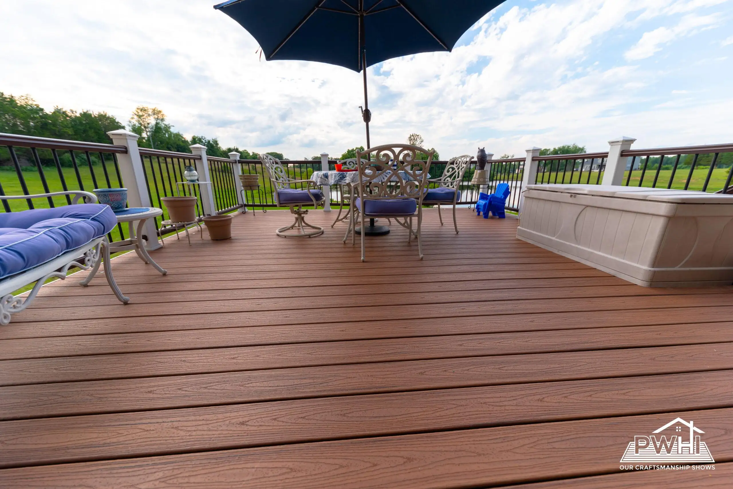 Why Prince William Home Improvement is the Right Choice for Your Deck 3 A deck made of composite material with black metal railings, featuring a round dining table and seating area with two lounge chairs. The deck is attached to a brick house with large windows.