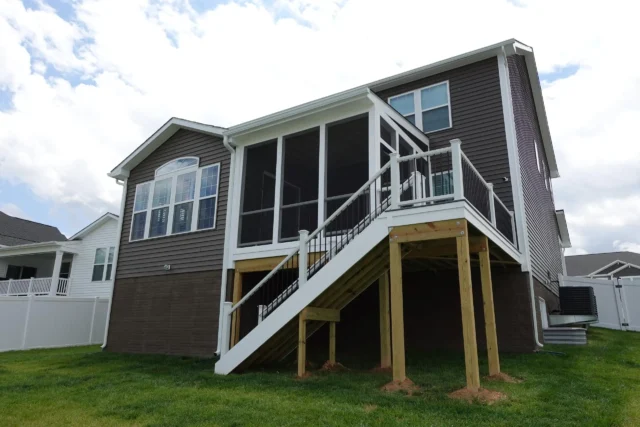 Deck Repair vs Replacement Detailed Guide A high-angle view of a brown-sided house with a white screen porch on the second level, a white staircase leading to the ground, and a brown composite deck with white railings.