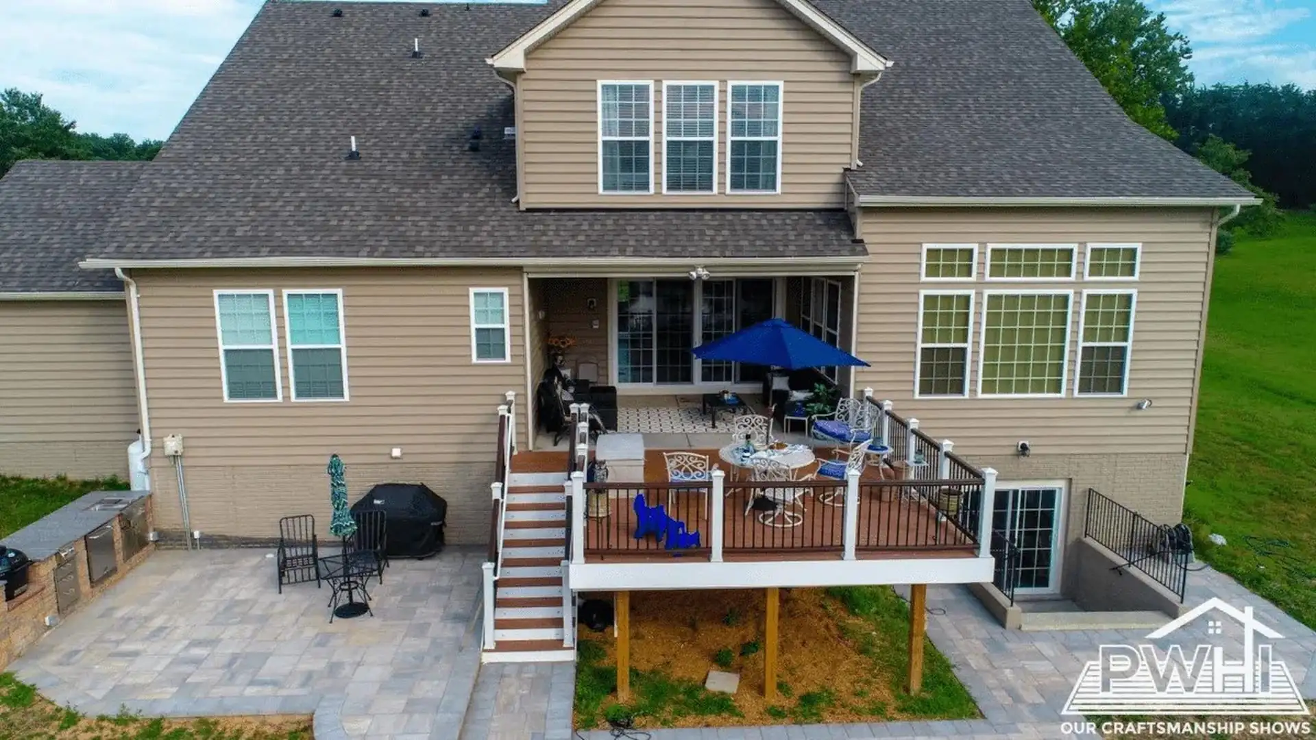 Aerial view of a custom outdoor living area featuring a ground-level paver patio, an integrated outdoor kitchen counter, and an elevated composite deck with white railings.