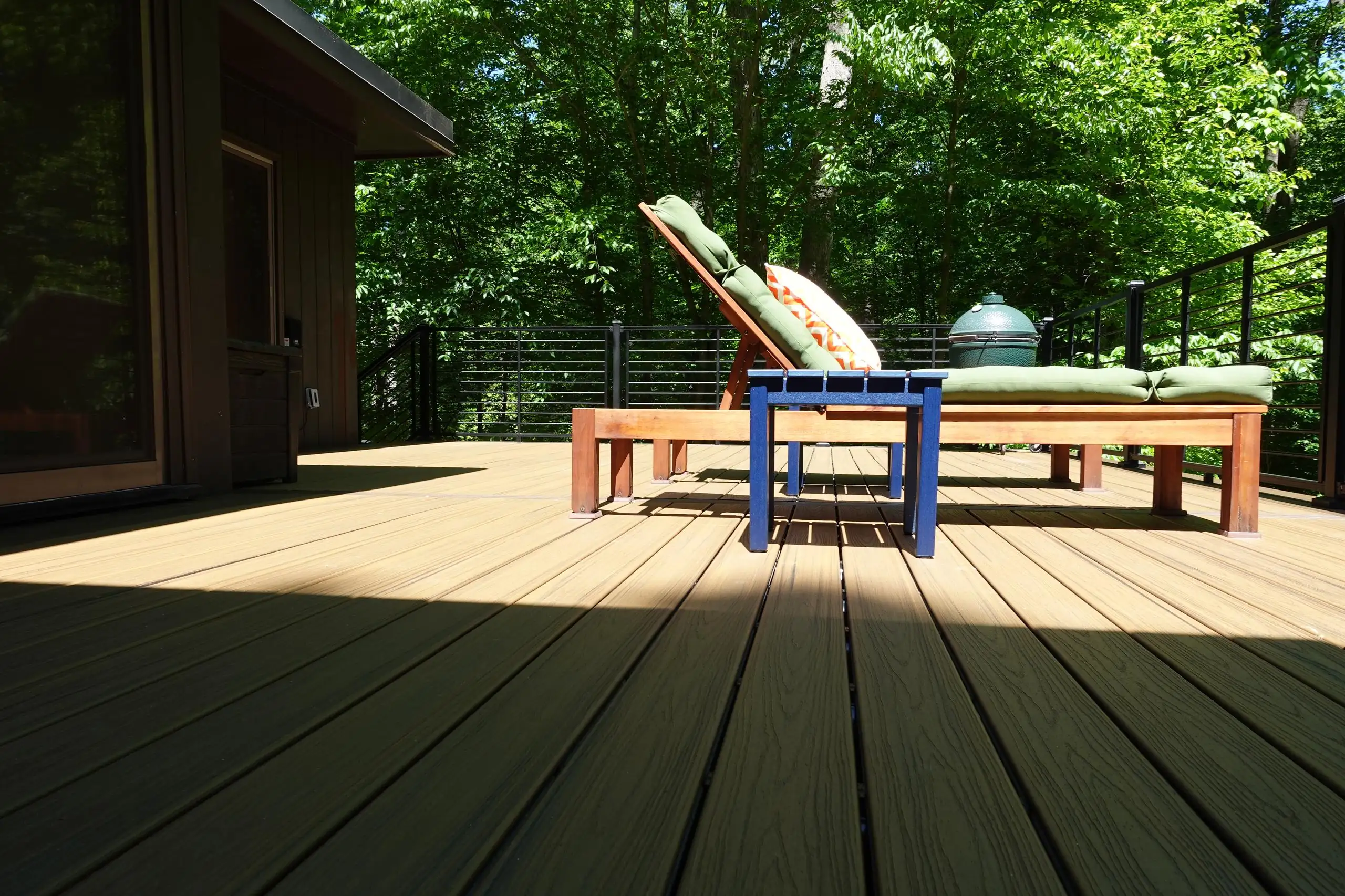 An outdoor deck with light gray composite decking and a white railing system with black balusters, attached to a house with gray siding.