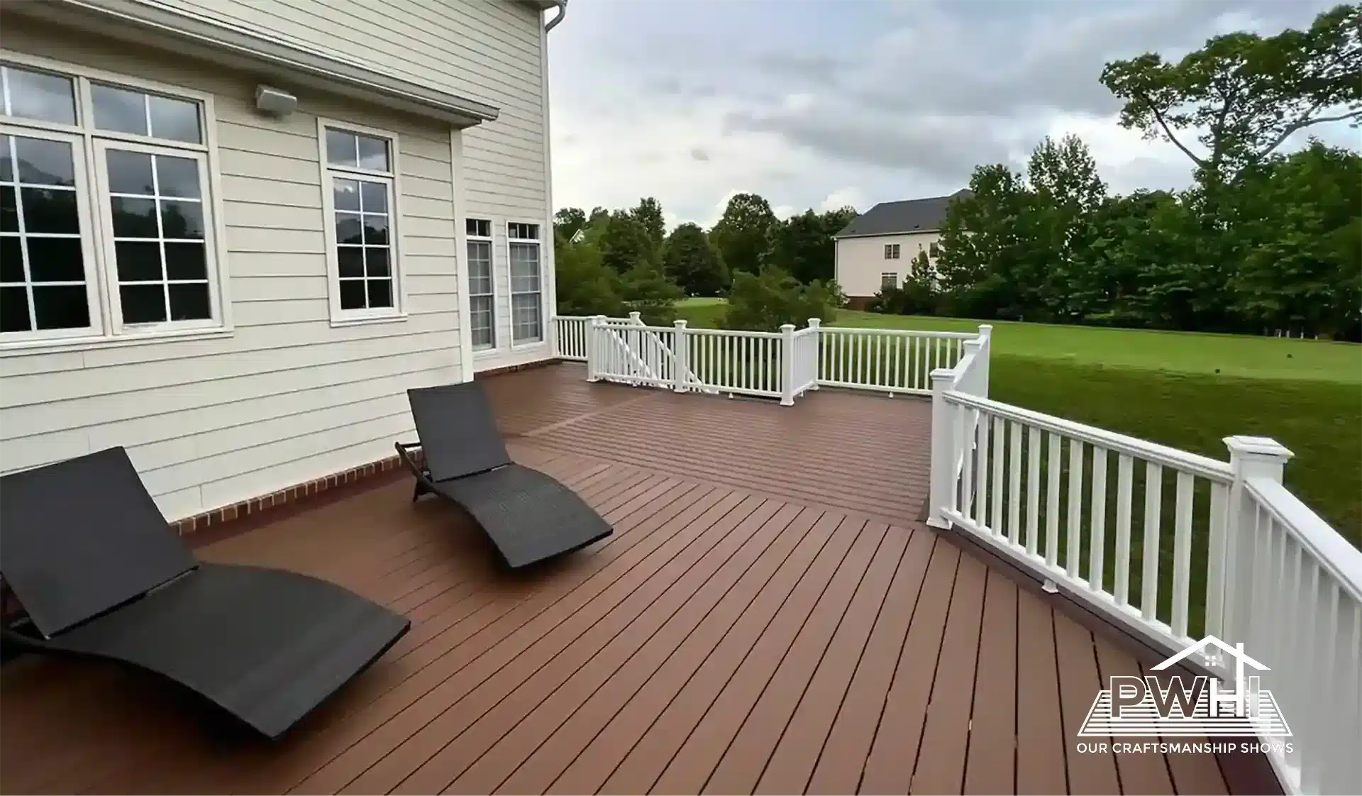 composite decking builder in fredericksburg va Large, elevated brown composite deck with white vinyl railings attached to a light beige house. Two black lounge chairs are on the deck overlooking a large green lawn. The image includes a "PWH OUR CRAFTSMANSHIP SHOWS" logo.