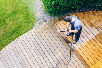 man cleaning the wooden deck with a power washer during Spring