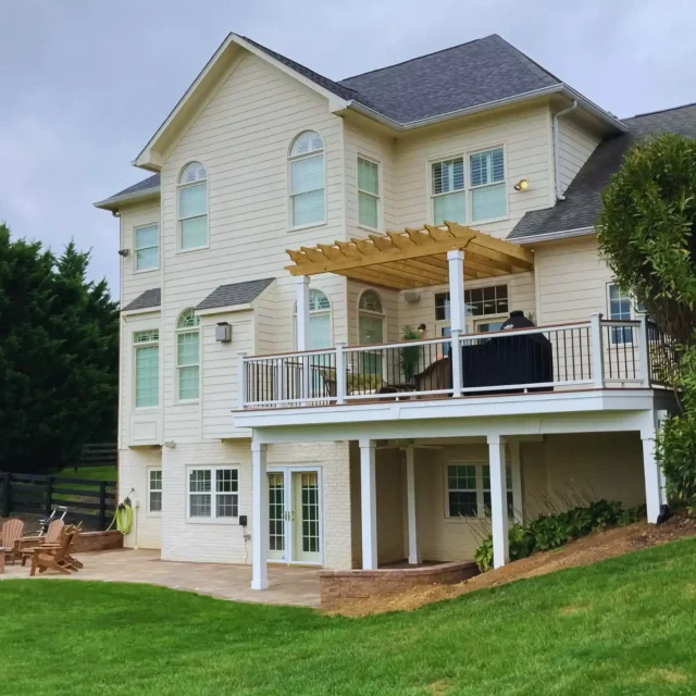 Custom raised deck with white posts, black railings, and a wood pergola attached to a home by Prince William Home Improvement.