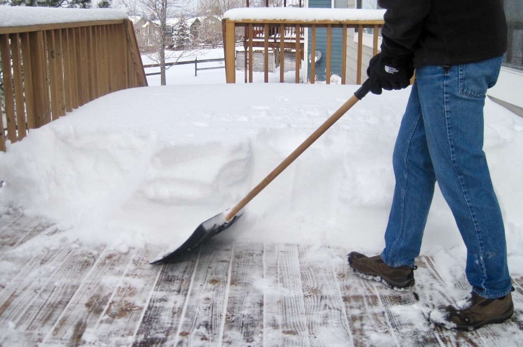 A homeowner shoveling snow away from a deck using a plastic shovel